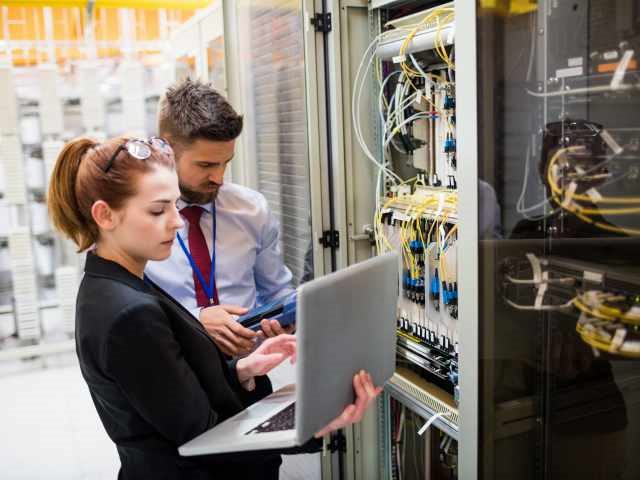 Technicians using laptop while analyzing server in server room