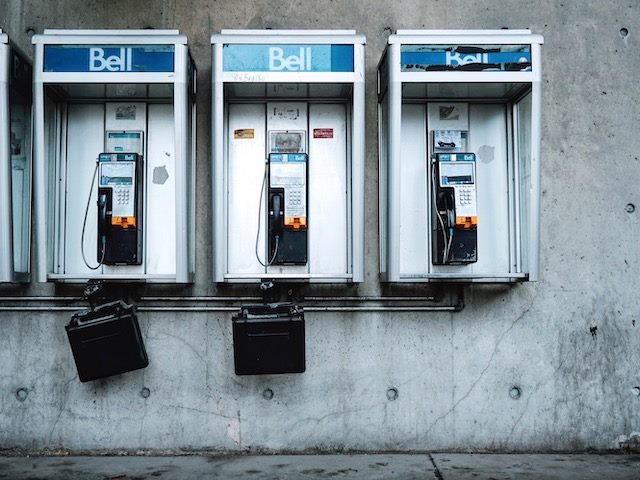 three decrepit pay phones in a row with telephone books attached