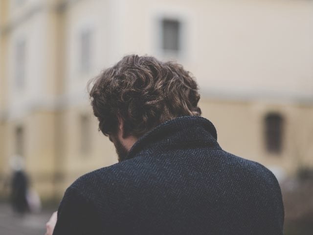 Shot from behind a man, with his head bowing toward the grounding