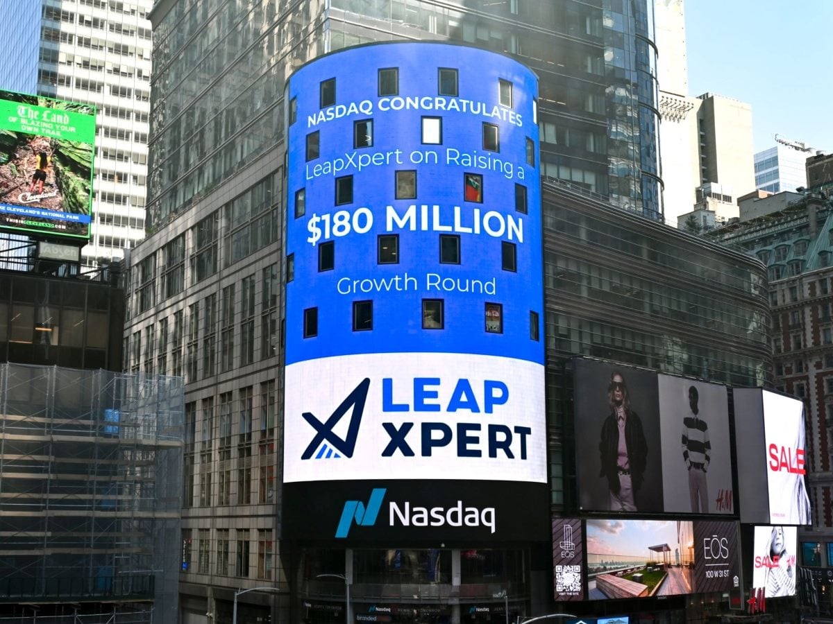 A large digital billboard on the Nasdaq MarketSite tower in New York City's Times Square congratulates LeapXpert on its $180 million growth funding round. The blue-and-white display features the LeapXpert logo, the funding amount in large type and Nasdaq branding at the base, surrounded by neighboring skyscrapers and retail advertising displays.