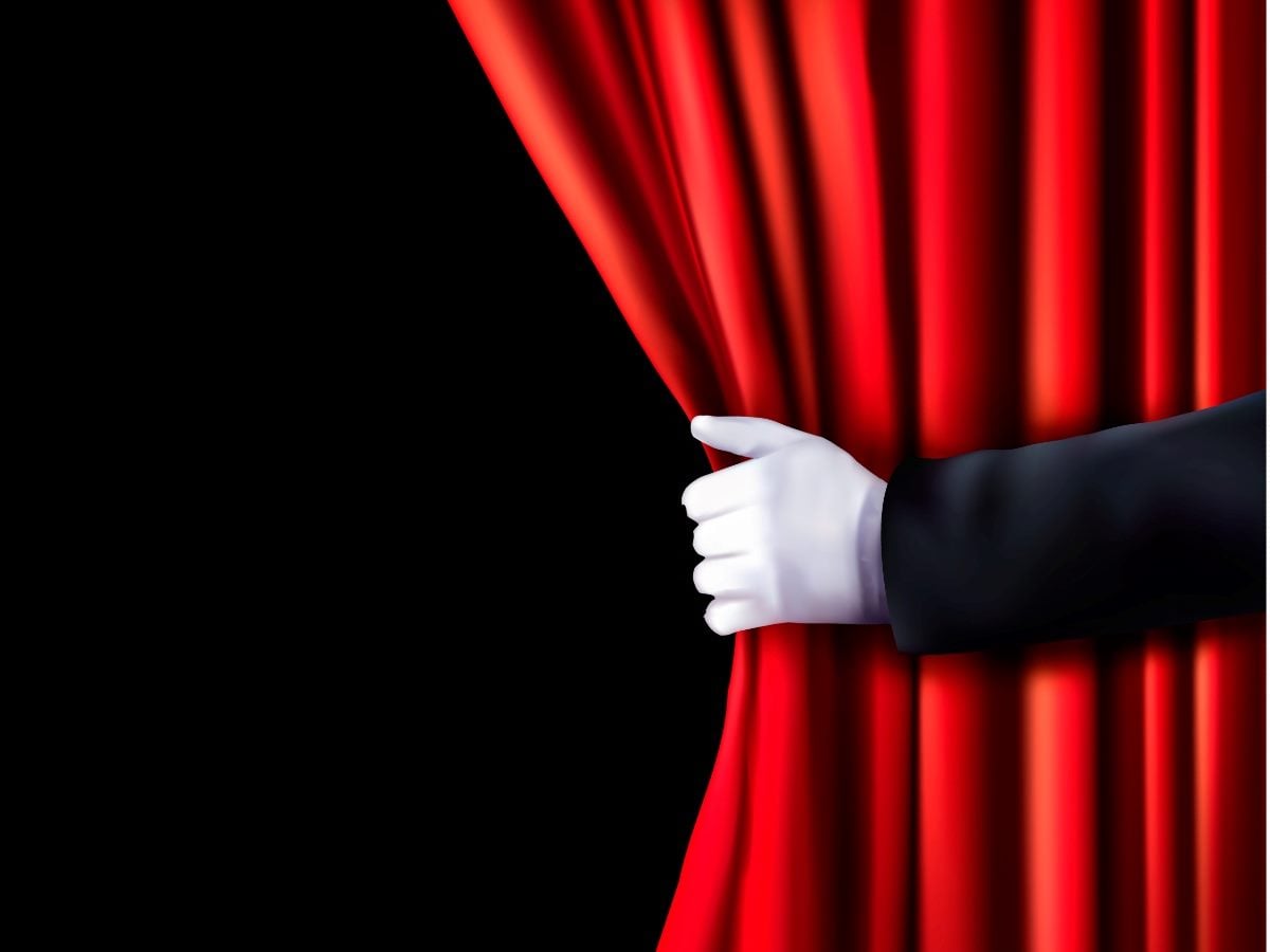 A red theater curtain is being pulled back by a white-gloved hand emerging from a dark sleeve, revealing a black empty space behind it. The image evokes a reveal, behind-the-scenes look, hidden insights or the unveiling of information.