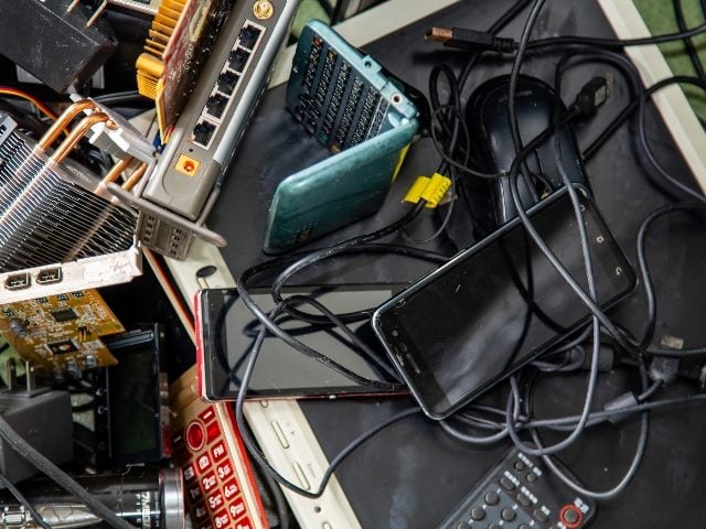 An assortment of e-waste is visible including a laptop and tablet in piece about the lack of digital sustainability and overconsumption. 
