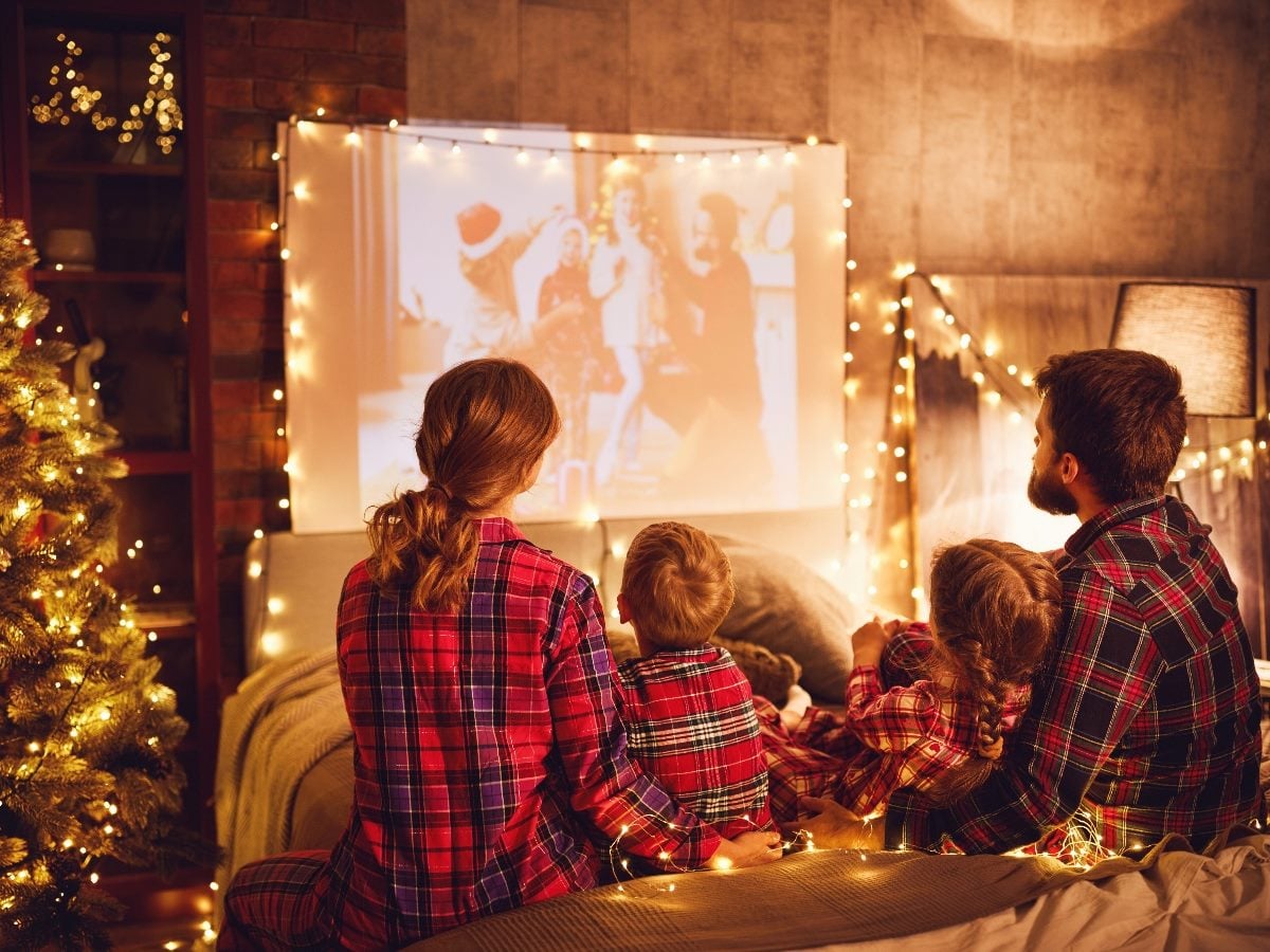 Family -- mother, father and two children -- watching projector with popcorn during Christmas.