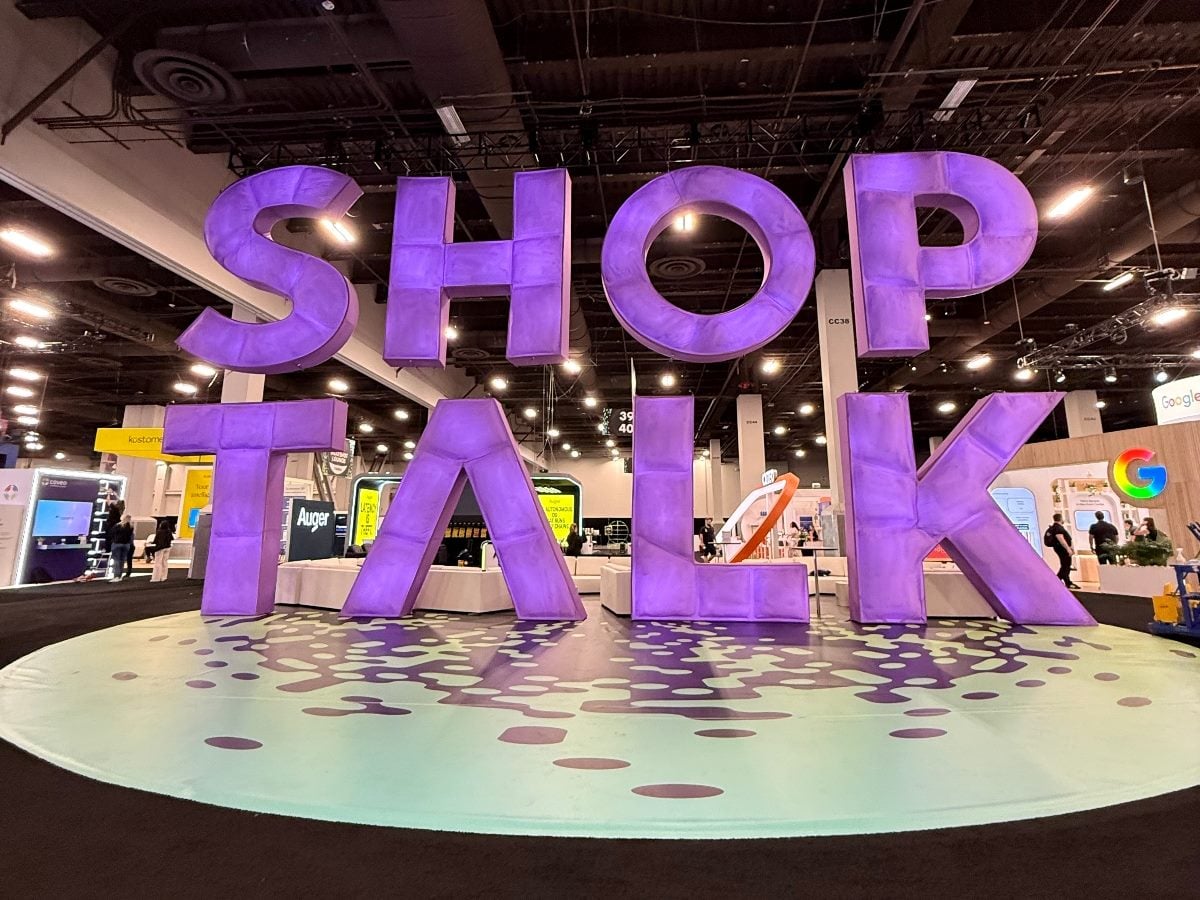 Large purple “SHOP TALK” installation on the show floor at the Shoptalk conference inside Mandalay Bay Convention Center, surrounded by retail tech booths and displays.