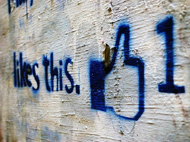 blue spray paint on while wall that says, "likes this" with the facebook thumbs up and a number 1 sign