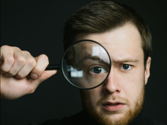 A man holding up a magnifying glass over one of his eyes - Monitoring trends concept