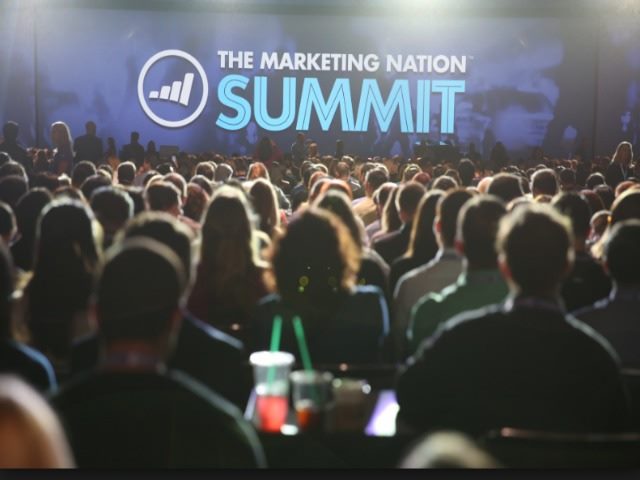 People in the crowd at the Marketing Nation Summit focus on the stage.