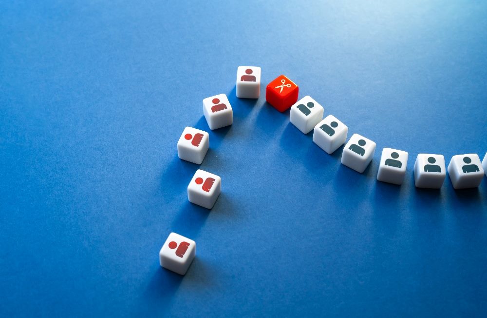 Cubes showing purple and blue people icons and one showing a pair of scissors show the impact of business cost-cutting on the customer expereince.