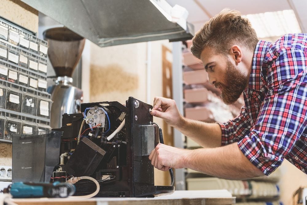 A person wearing a plaid shirt works to repair a broken coffee machine in a piece about Kentico Partner Day and the digital experience platform industry.