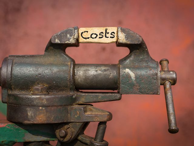 A vice tool squeezing a piece of wood with the word costs on it