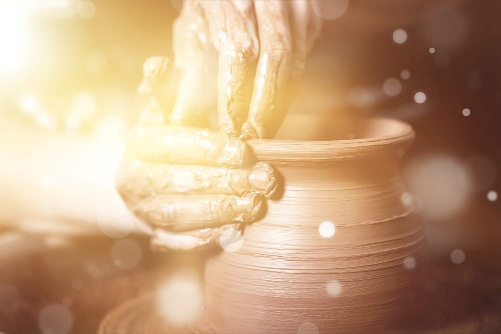 A ceramic artist transforms raw clay into a pot with their hands and is highlighted by golden lighting in piece about digital customer experience transformation.