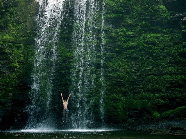 standing behind a waterfall with arms raised