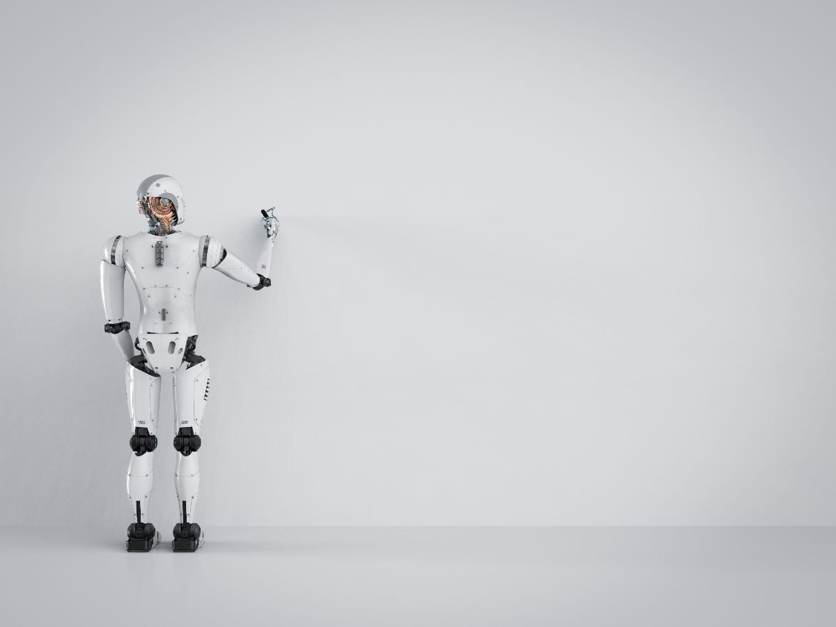 Minimalist image of a white humanoid robot standing against a blank gray wall, reaching one hand toward the empty space in front of it.