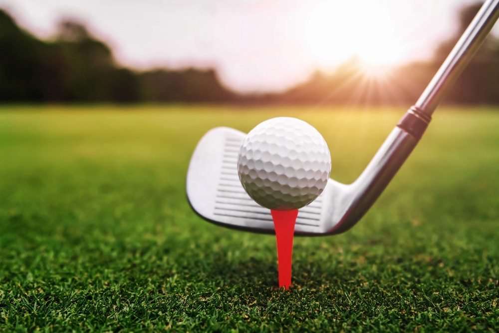 Close up golf club and golf ball on a red tee on green grass with sunrise background in story about customer experience and employee experience in golf venues.