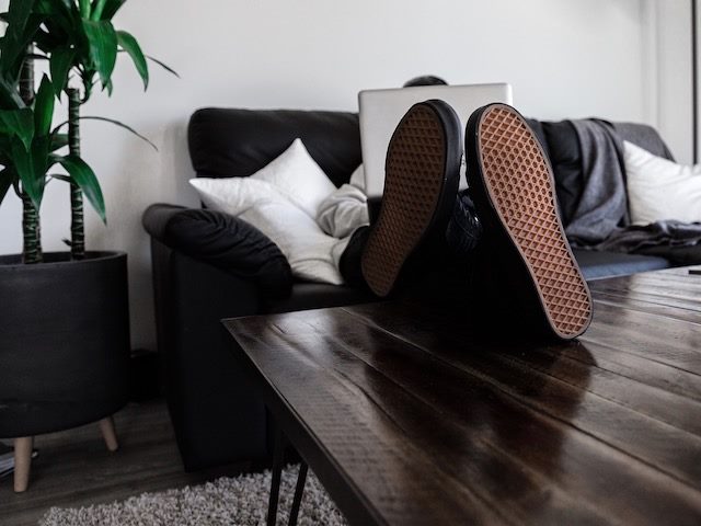 close up of feet on a coffee table as person works on laptop sitting on couch at home