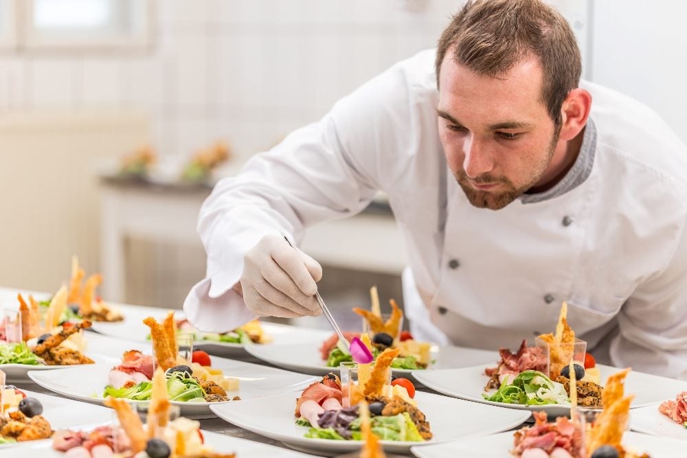 A chef in a white double breasted jacket leans over to meticulously garnish elaborately made appetizers in piece about B2B content.