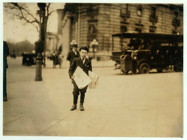 Newspaper boy staring at the camera holding his newspapers.