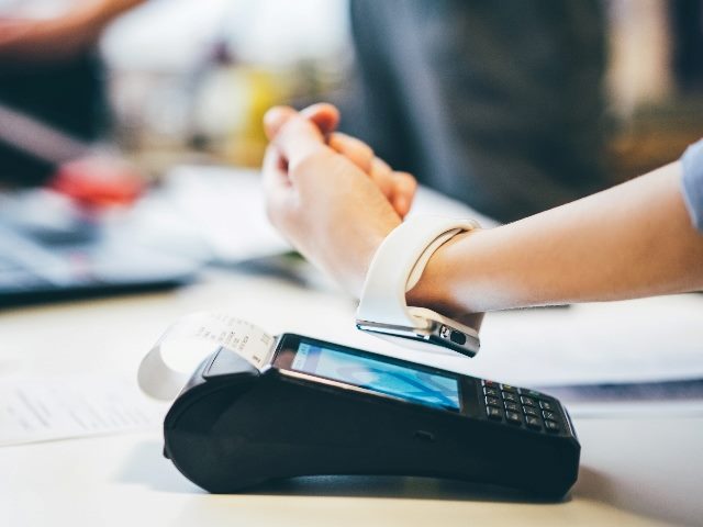 Someone using a smart watch to pay, showing only the person's wrist and arm paying on the device. 