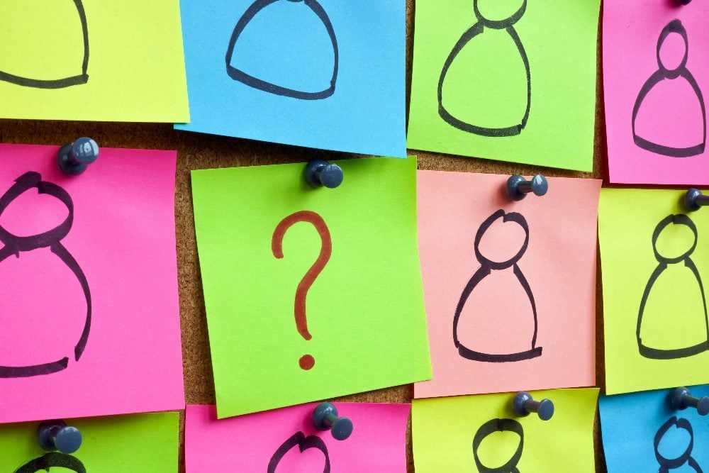 Pinned colorful stickers in neon pink, green and blue with simple drawings of people on them and a question mark.in the center sticky note in piece about quantitative and qualitative data research.