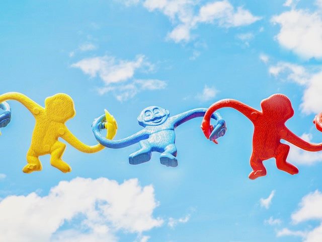 barrel of monkey toys holding hands, yellow monkey, blue monkey, red monkey
