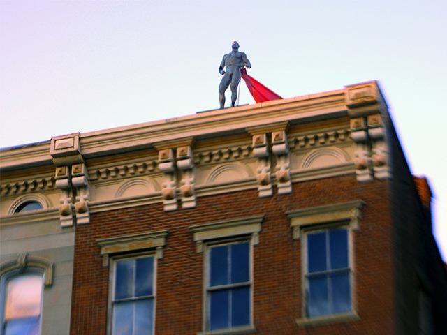 Superhero standing atop a brick building.