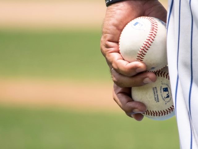 baseball player holding two baseballs on the pitcher's mound