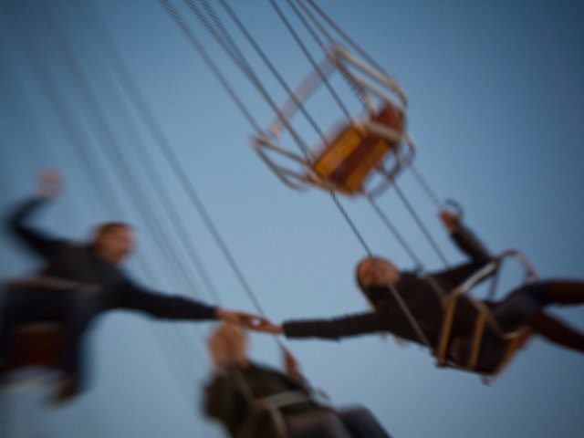 couple on swing ride grabbing hands in mid-air