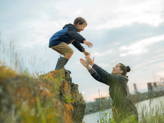 Mother waiting for her child to jump off a rock so she can catch him, symbolizing trust. 