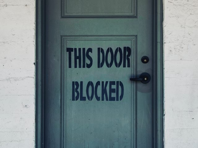 the words "this door blocked" painted on a closed door