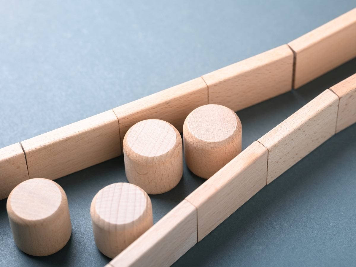 Light wooden blocks and rails arranged in narrow channels on a blue surface, illustrating constraints, structure and controlled pathways.