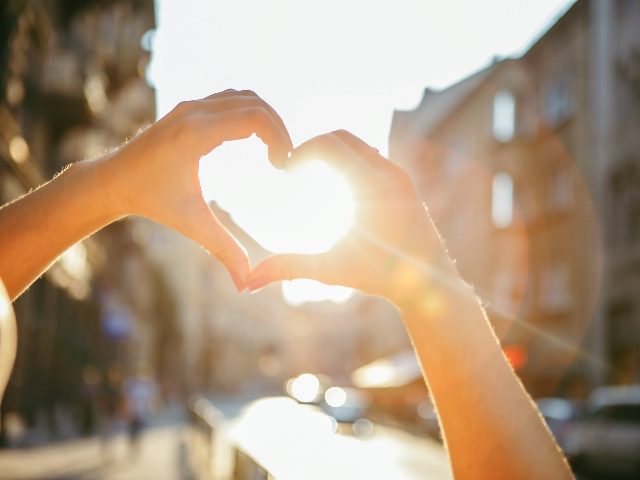 Woman hands in heart love shape symbol at sunset. 