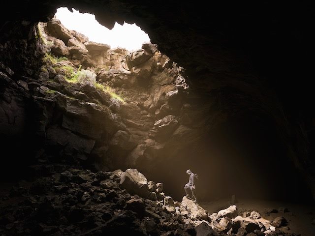 person standing  in a cave, bathed in light from an opening above