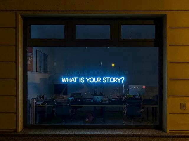 A large glass window with a neon sign that says " What Is Your Story?"
