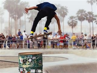 skateboarder doing an ollie over a trash can as people watch