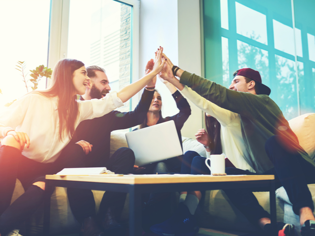 Female and male coworkers celebrating a successful campaign, giving high five during a meeting.