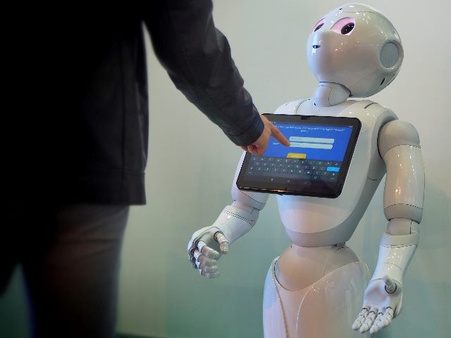 Robot Pepper by SoftBank Robotics, a humanoid assistant for better customer experience. The robot has a touch screen on its chest and is looking up at a man pressing a button on the touch screen.