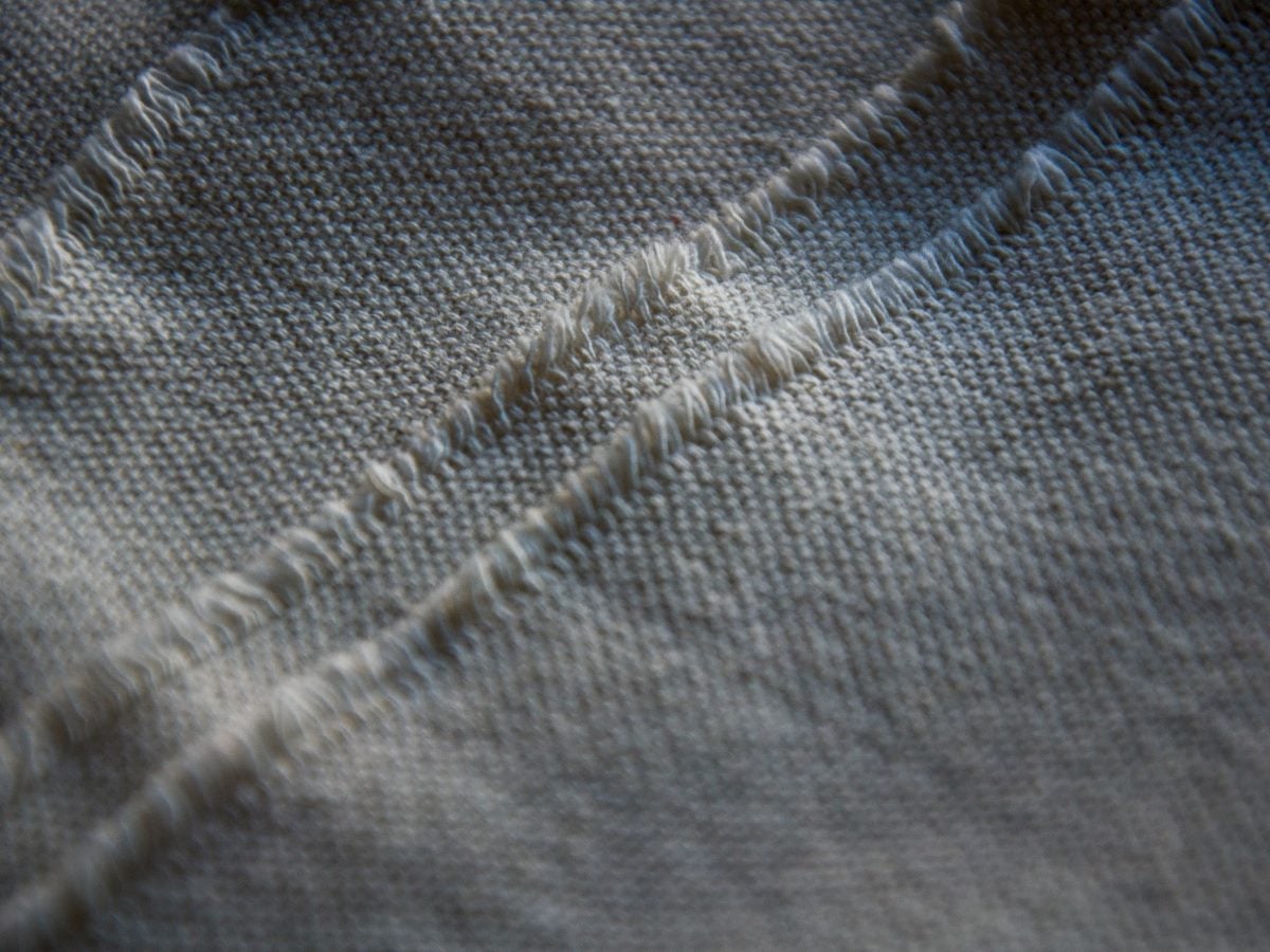 Close-up of frayed seams on coarse beige linen texture.