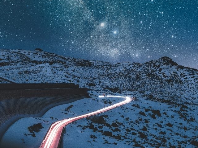 A street passing through snowy mountains lit up by car lights.