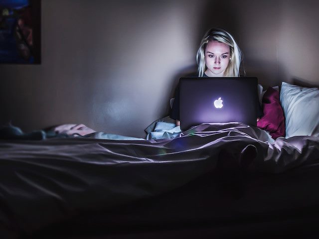 woman in bed in a dark room looking at a laptop