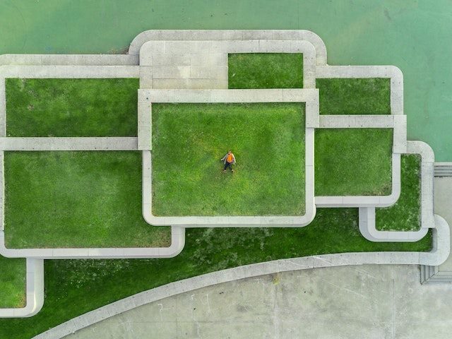 architectural platform with multiple components covered in grass. a human laying down at the center