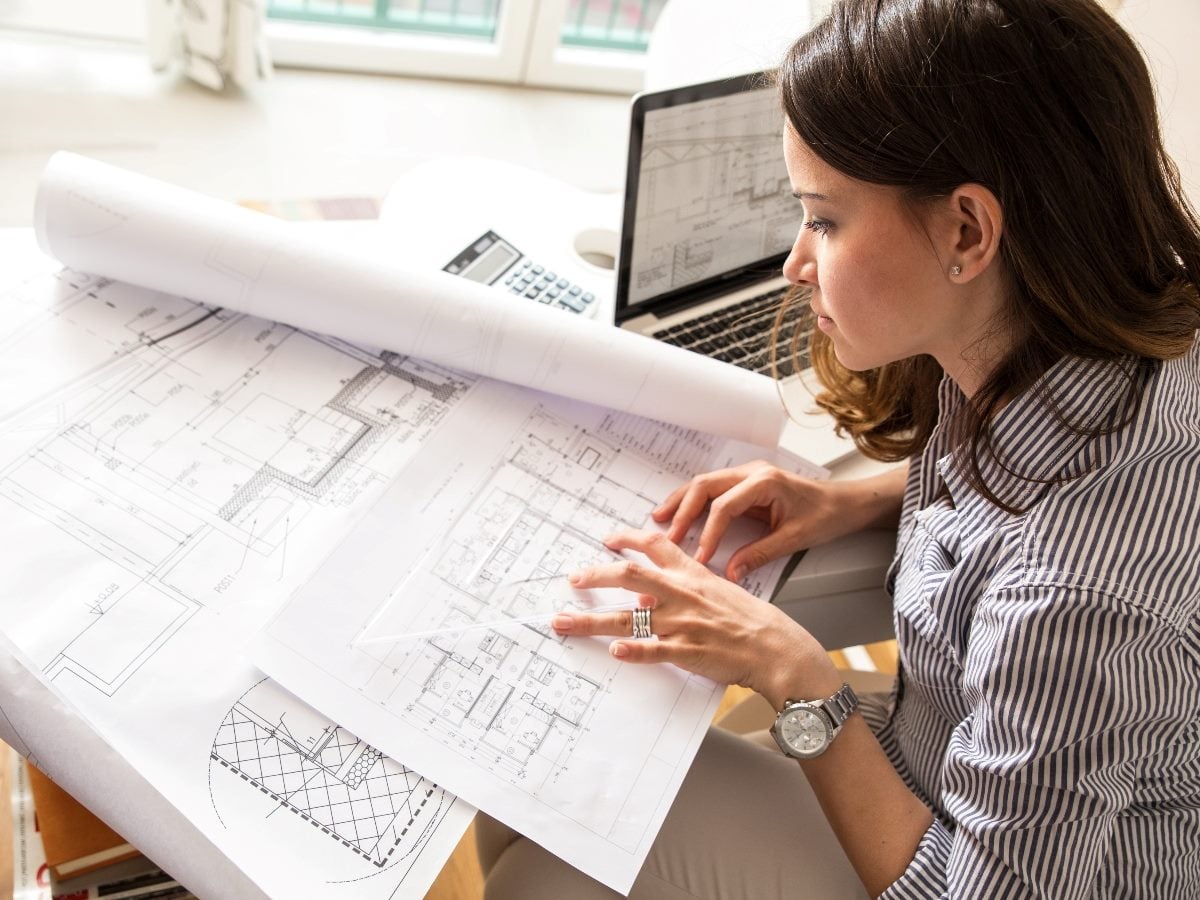 Business professional reviewing architectural blueprints and diagrams at a desk beside a laptop, visually representing the growing role of CMOs as architects of customer data infrastructure and marketing systems.