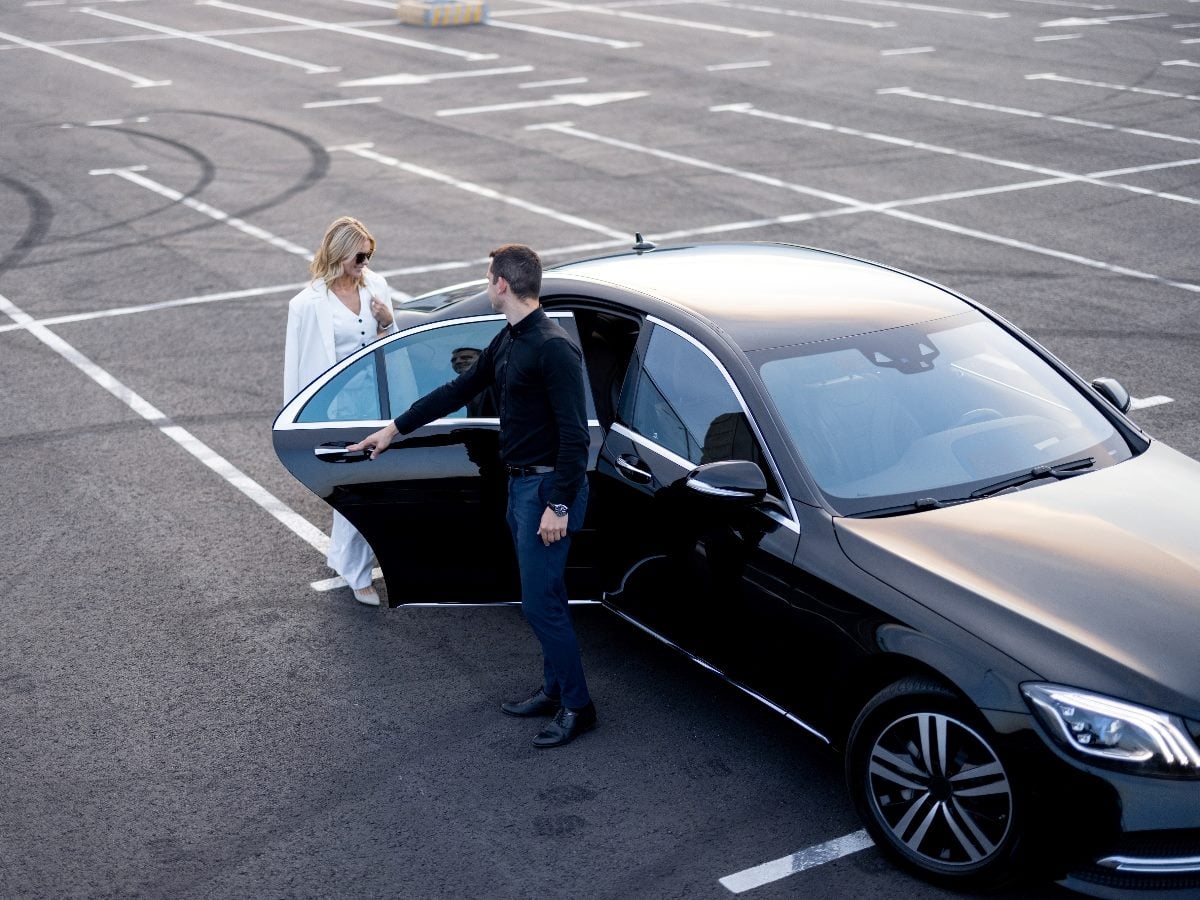 Chauffeur helps a businesswoman to get out of a car on parking lot, view from above.