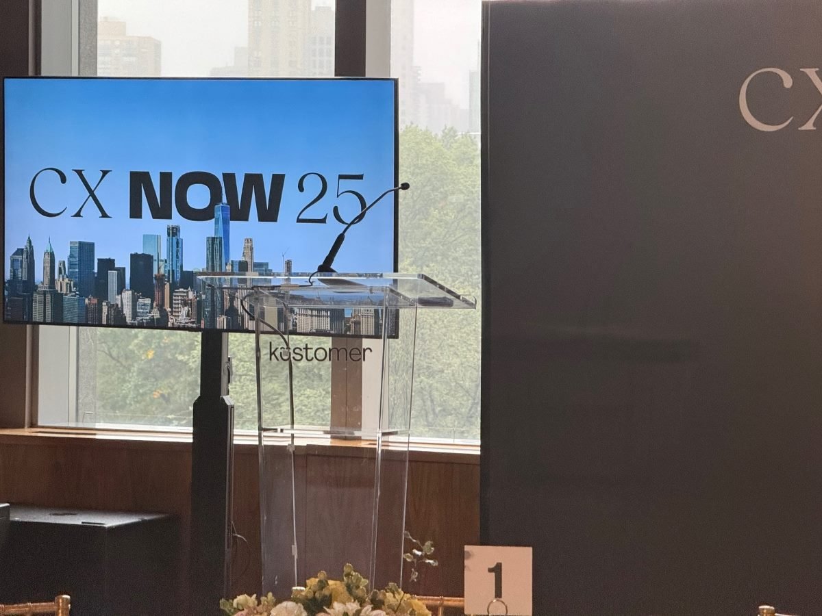 tage setup at Kustomer’s CX NOW 25 in New York—podium and mic beside a screen showing “CX NOW 25” over a city skyline.