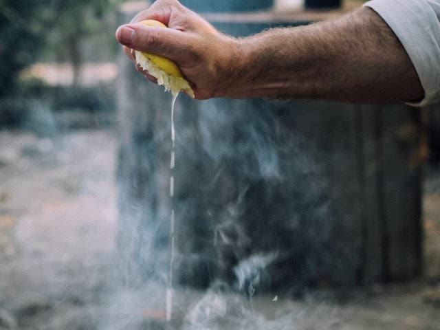 a hand squeezing  a lemon over an  open flame