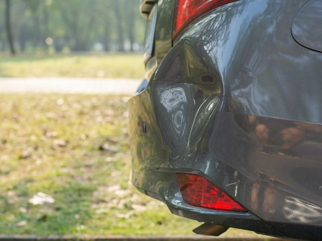 Broken rear bumper on a parked gray car. 