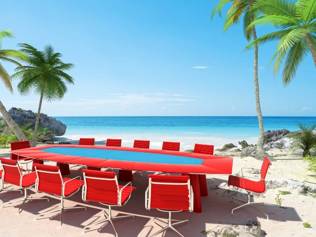 Bright red and blue table with empty red chairs on a a beautiful sandy beach with palm trees, symbolizing the difficulty of getting customers to attend customer advisory board meetings 