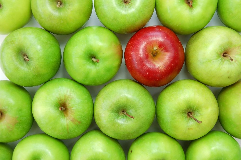 One red delicious apple in a sea of green Granny Smith apples suggesting the need for an exceptional CX Digital Content Strategy to stand out in a crowd.