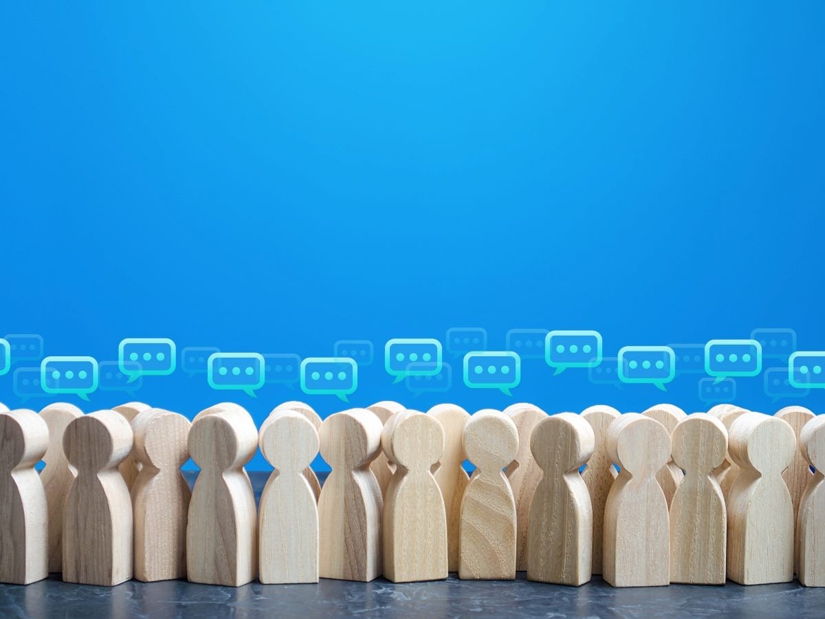 A row of wooden peg-style figures standing side by side against a blue background, with translucent chat bubbles floating above them, symbolizing group communication or survey feedback.