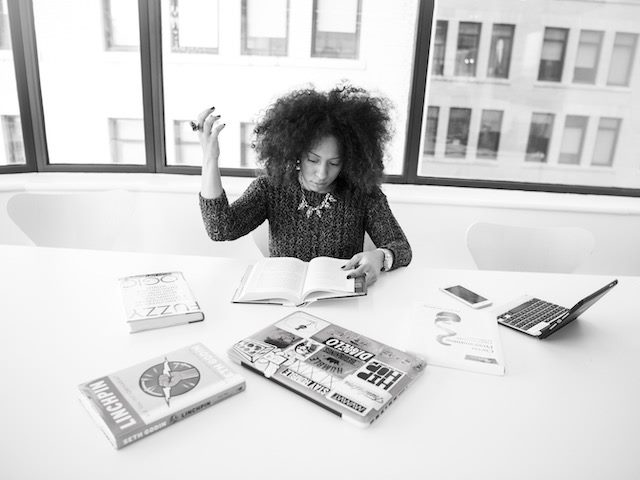 woman  studying with a number of open books and laptops around her