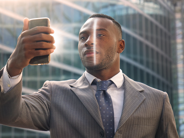 A businessman in a city environment using facial recognition technology to access an app on his smartphone